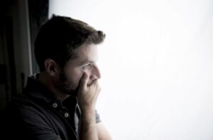 A man looking out a window with a worried expression