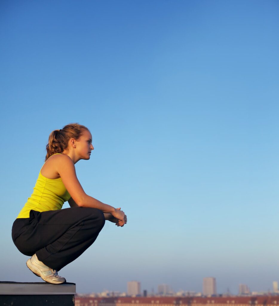 A woman crouching near a ledge overlooking a city