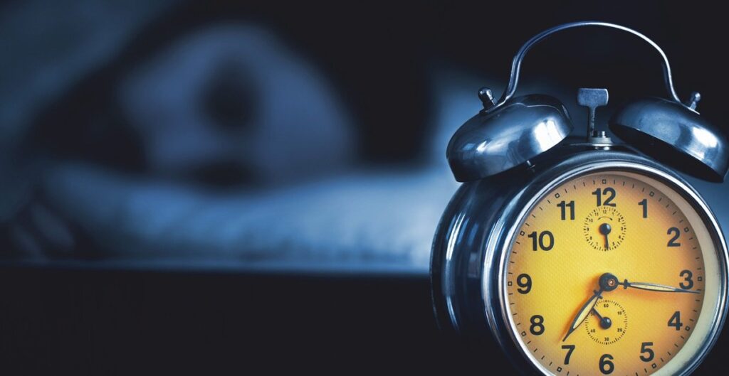 Someone sleeping in a bed with a clock next to them